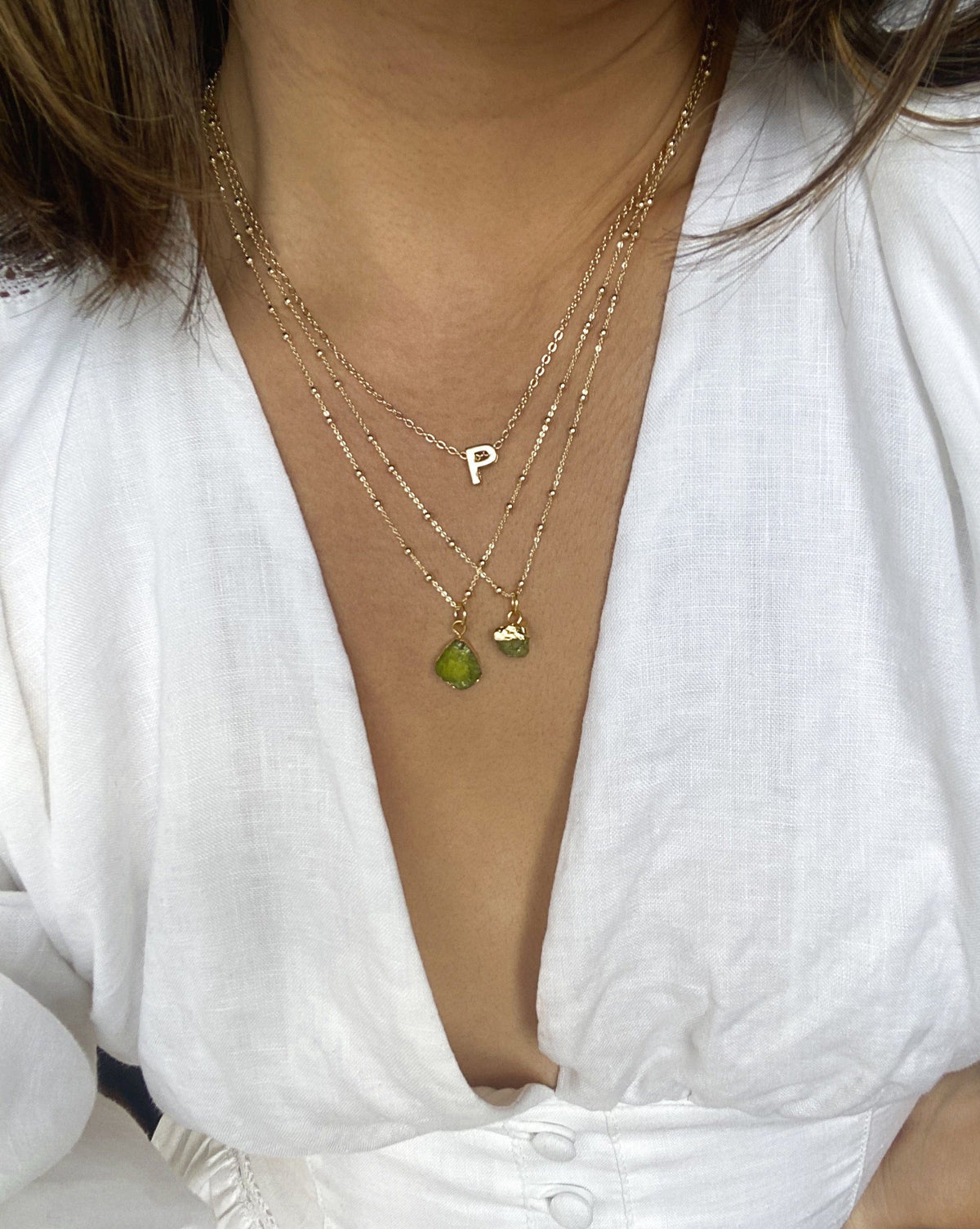 2 birthstone necklaces stacked with an initial necklace on a woman wearing a white dress