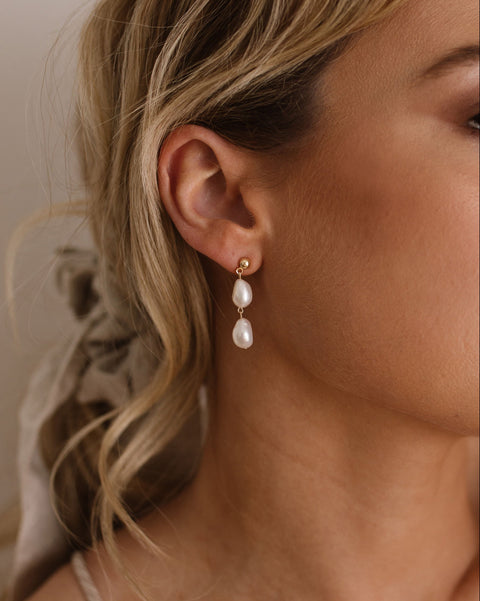 Close-up of a woman wearing pearl earrings with a neutral background
