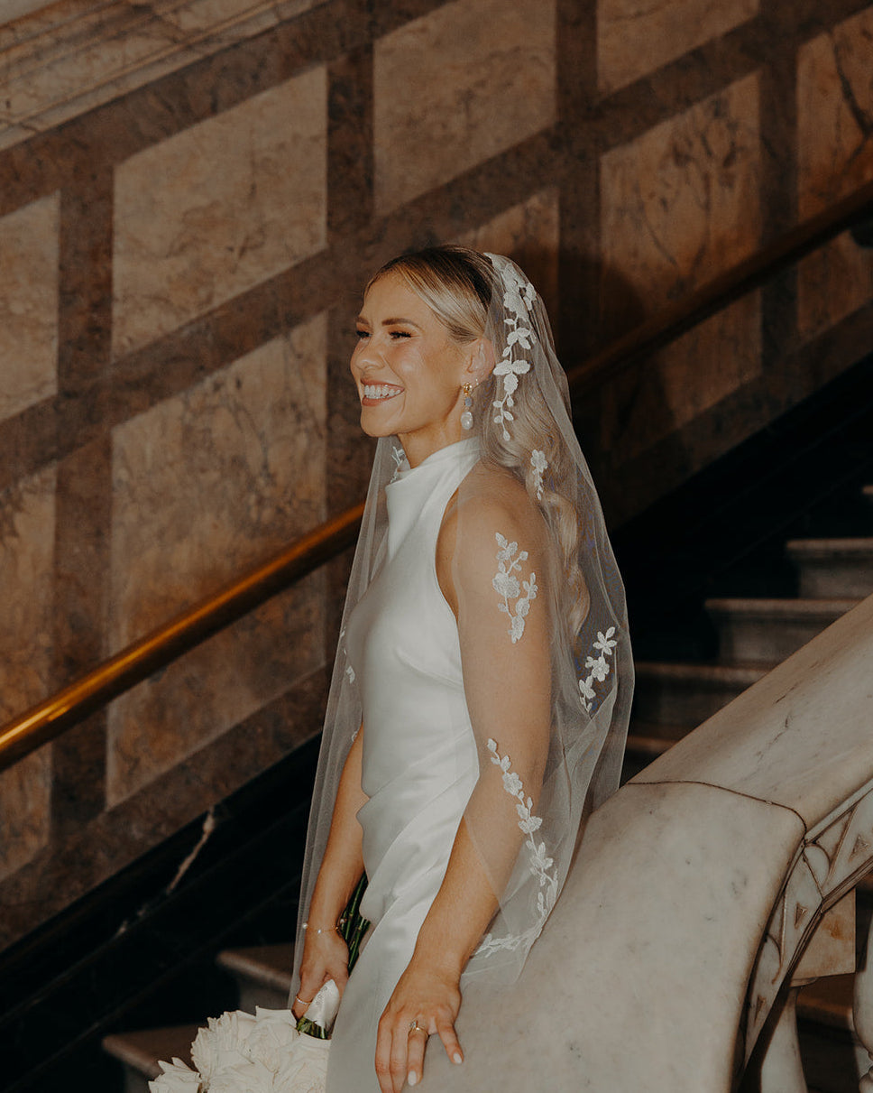 Bride in a white wedding dress with a floral veil standing on a staircase.
