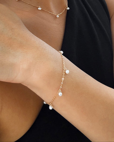 Woman wearing a pearl bracelet, necklace, and earrings against a white curtain background