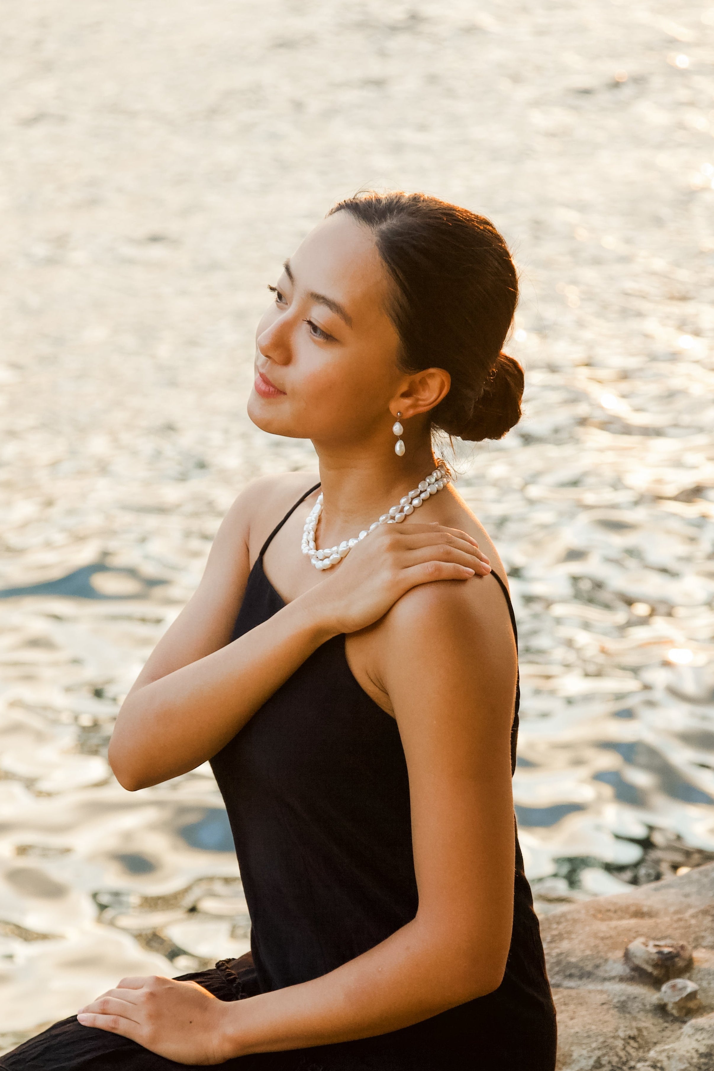 Woman in a black dress sitting by a body of water, with double drop pearl earrings and double tier pearl necklace.