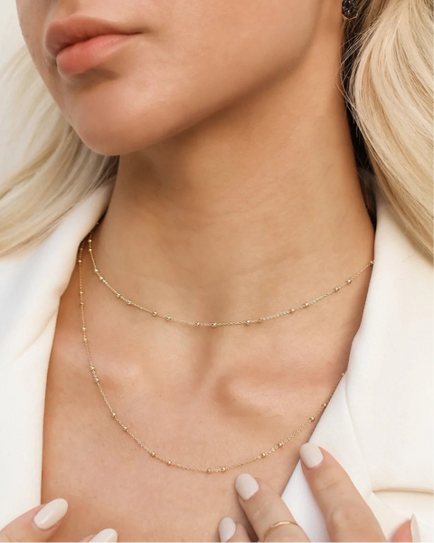 Close-up of a person wearing a delicate gold necklace with a blurred background