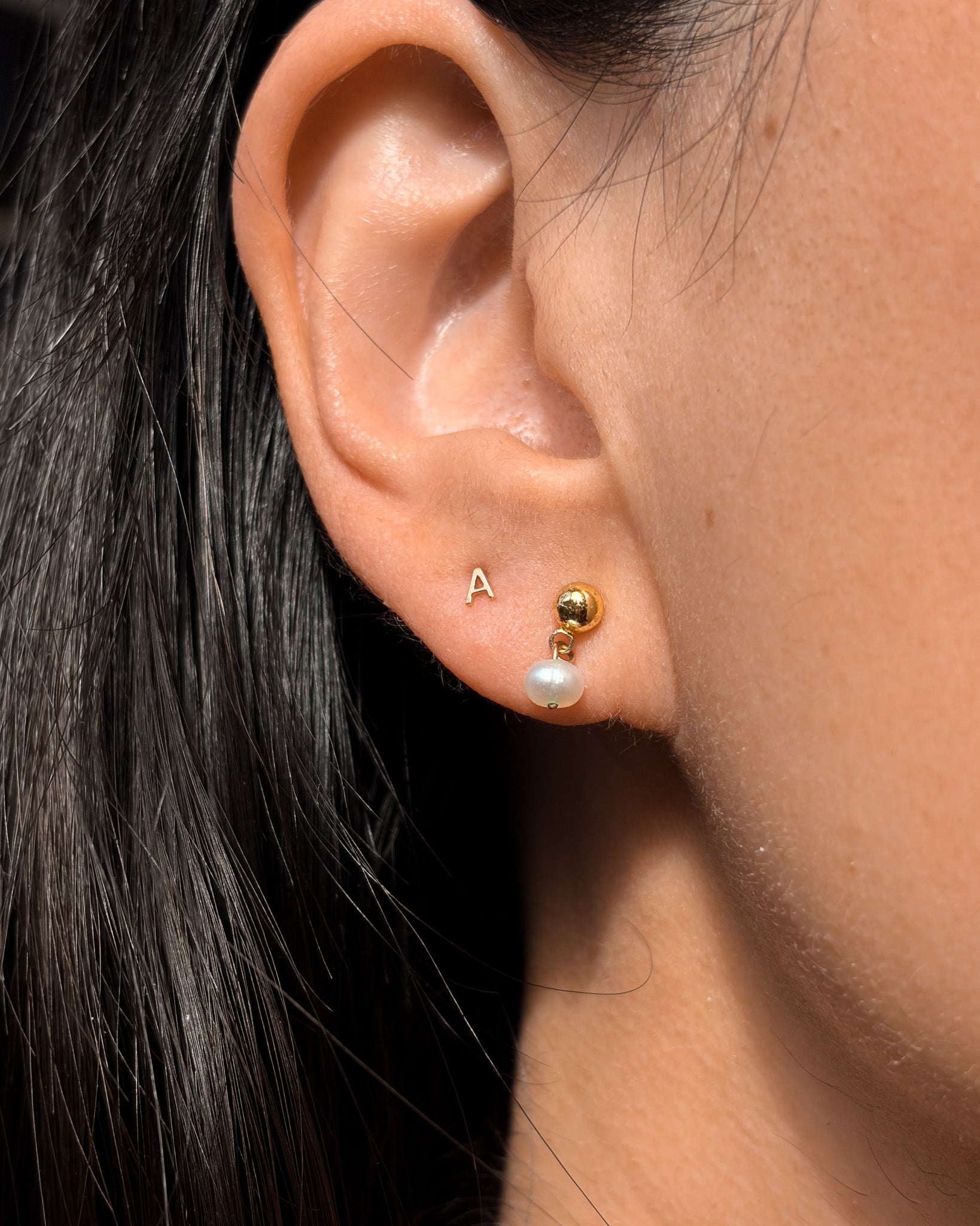 Close-up of an ear wearing gold and pearl stud earrings.