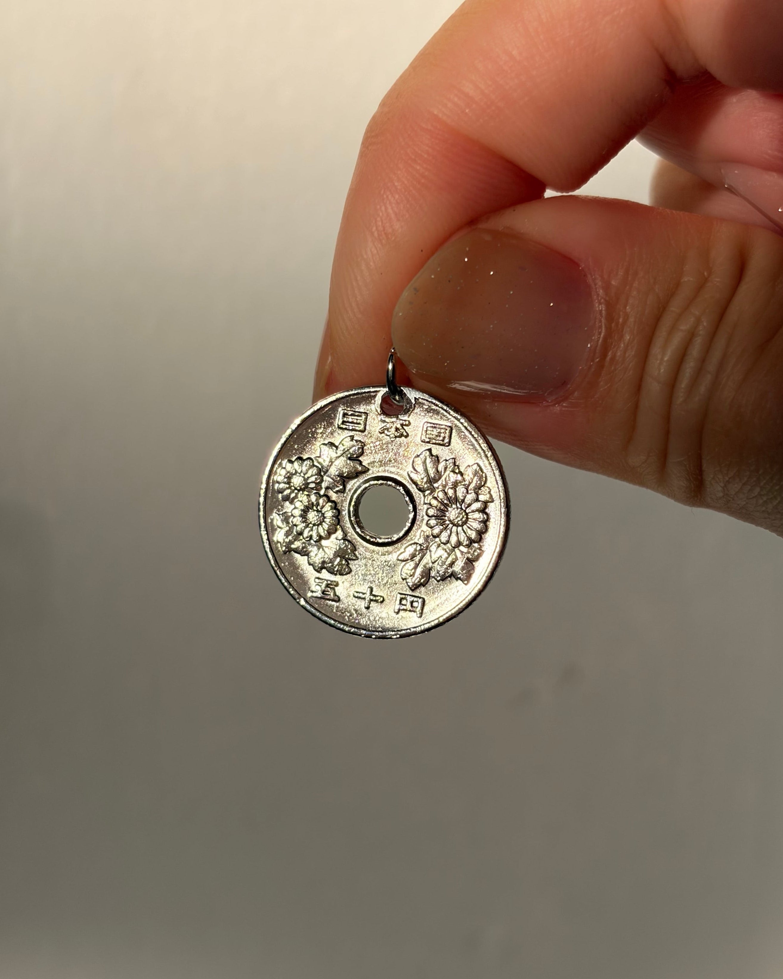 Hand holding a small round metallic object with intricate designs on a plain background