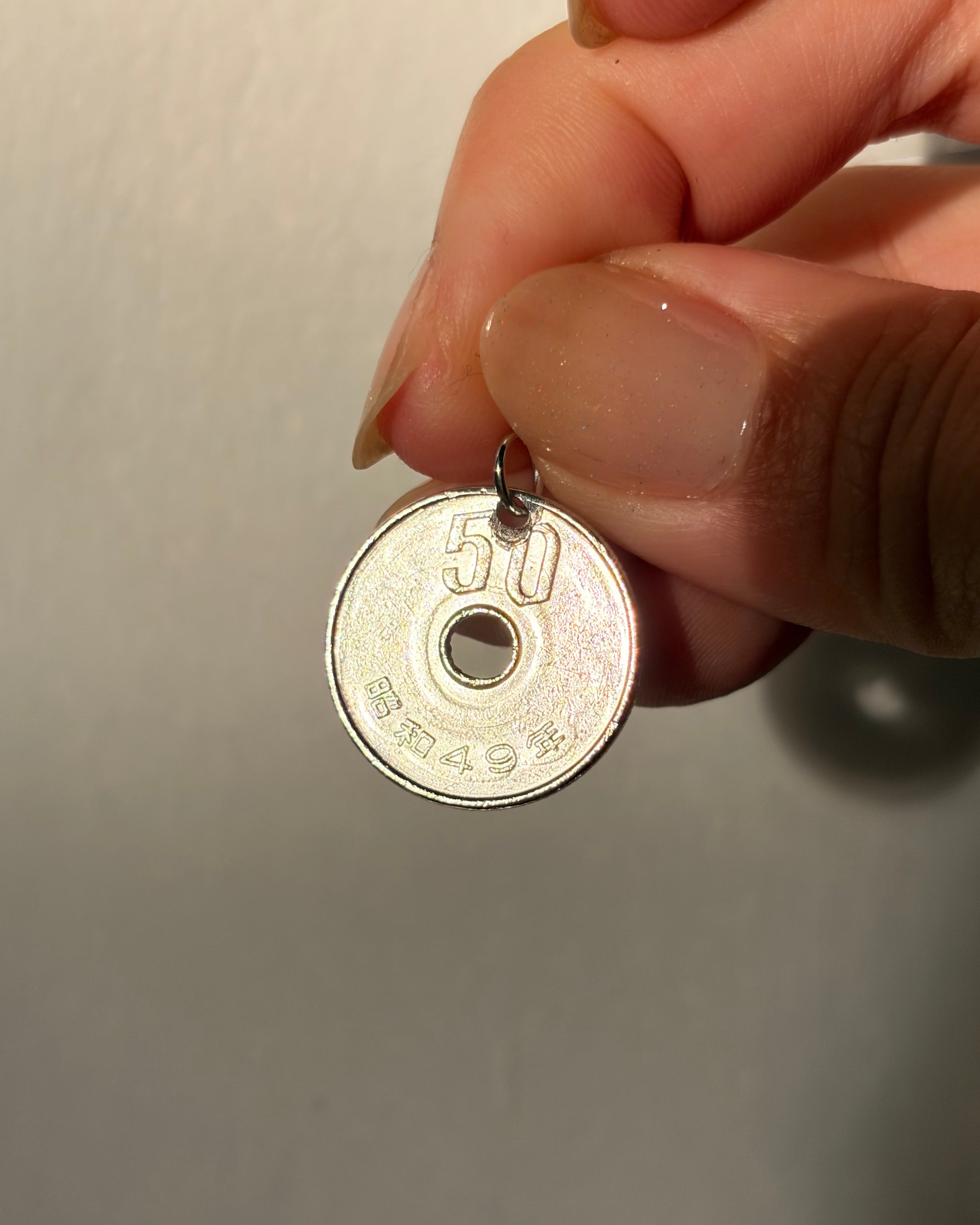Hand holding a small metallic object with visible text on a plain background
