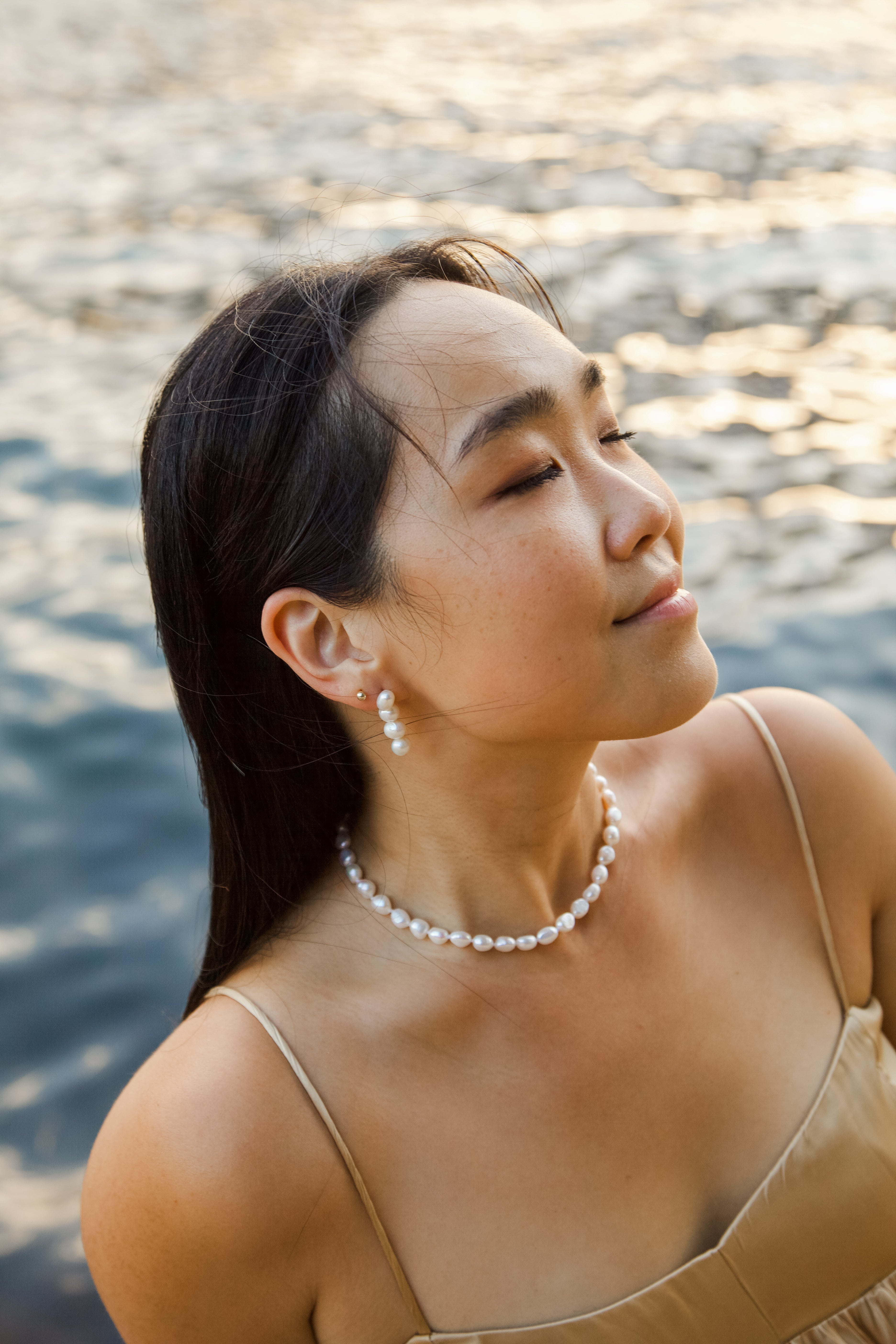 Woman wearing a pearl necklace and earrings by a body of water